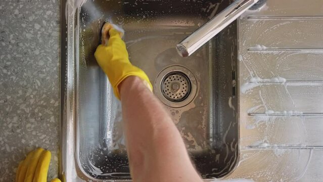 Static top down shot of a male scrubbing the kitchen sink with a sponge