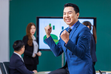 Millennial Asian professional successful businessman ceo entrepreneur in formal business suit smiling in meeting room showing fist up celebrating working with male and female colleagues discussing.