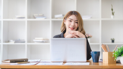 Portrait of businesswoman sitting at working desk with laptop  and smiling to camera.