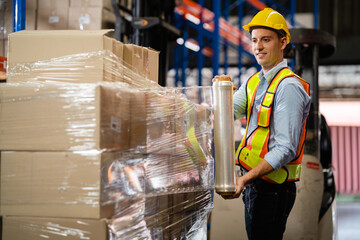 Male worker wrapping parcel in stretch film on cargo in large factory warehouse Logistics and...