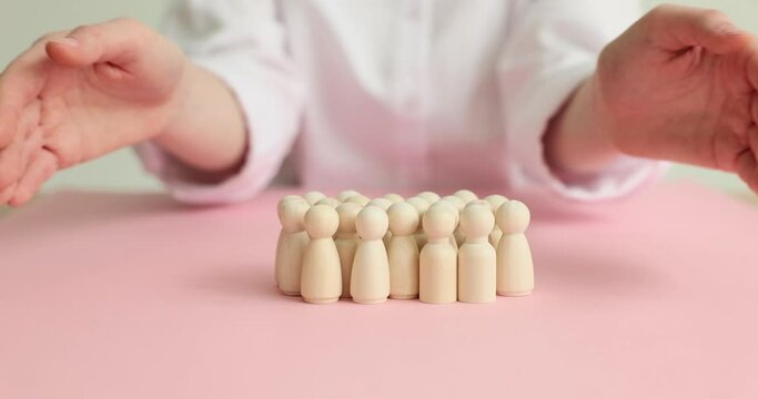 Female hands close wooden dolls on the table, close-up. The concept of community protection,