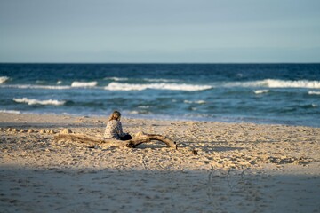 Mature age Woman sitting on the beach looking out to sea Contemplating life in the evening sunlight. White sand a crashing waves
