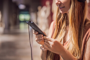 Portrait of contemporary young woman looking at sculptures and listening to audio guide at museum exhibition