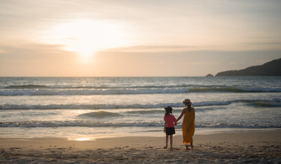 Fototapeta na wymiar Young mother with her child walk on the beach of a beautiful coast at the silhouette sunset.