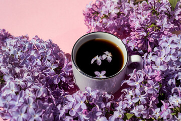 Obraz na płótnie Canvas A cup of black coffee on the table with a branch of lilac, top view. Coffee and different lilac flowers. Flower arrangement of beautiful lilac flowers with a cup of coffee. Selective focus.