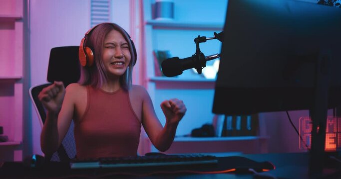Footage of Young Asian esport woman gamers playing online video games on the computer with neon light at home. Attractive girl gaming player feels enjoy technology broadcast live streaming.