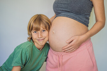 Young beautiful pregnant woman and eldest son. The cute boy leaned his ear against his mother's belly. Expecting a baby in the family concept. Preparing an older child for a younger one