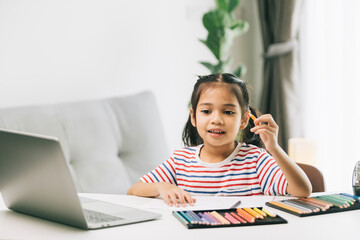 Naklejka premium Cute asian child girl drawing with color pencils at home