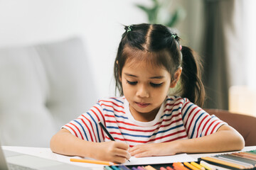 Naklejka premium Cute asian child girl drawing with colorful pencils at home
