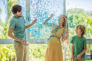 It's a boy. Expectant parents mother, father and their elder son are having a gender reveal party. A married the couple burst the balloon and the blue confetti flew out. Family, pregnancy and prenatal