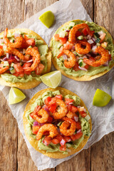 Tostadas with juicy shrimp, creamy avocado guacamole and tangy salsa closeup on the wooden table....