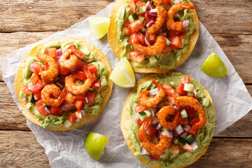 Freshly made shrimp tostadas topped with guacamole, onion, tomatoes, and cucumbers closeup on the wooden table. Horizontal top view from above