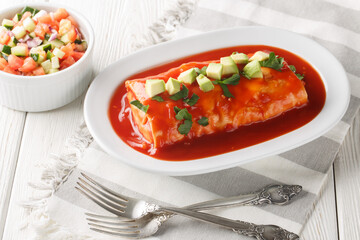 Wet burrito recipe made with flour tortillas filled with ground beef, refried beans, and chiles closeup on the plate on the wooden table. Horizontal