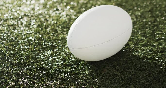 White rugby ball on sunlit grass with copy space, slow motion