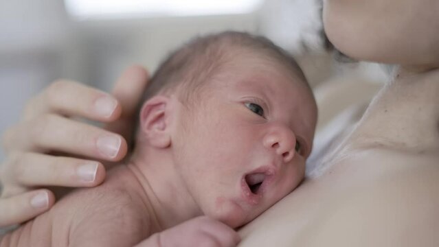 Adorable Newborn Baby Boy sitting on mother chest. Skin to Skin. Close up