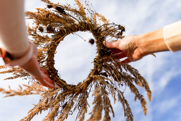 A wreath of a wild meadow flower in the hands of a girl against the sky. Summer solstice day,...