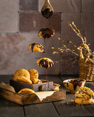 Homemade chocolate chip cookies with dripping chocolate sauce, captured in a creative flying composition. Rustic wooden surface, warm tones, and dessert styling create a cozy bakery atmosphere.