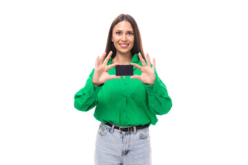 pretty well-groomed brunette long-haired young woman in a green shirt holding a bank card mockup on a white background with copy space