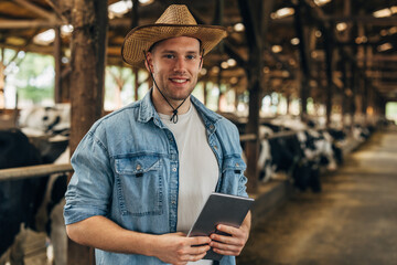 Portrait of a handsome farmer standing in a stable with tablet.