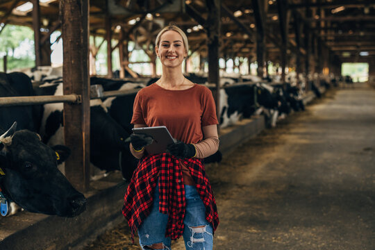 A happy female farmer standing in a stable with a tablet.