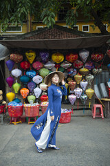 Tourist woman is wearing Non La (Vietnamese tradition hat) and looking colorful lanterns on the old street of Hoi An Ancient Town - UNESCO World Heritage village.