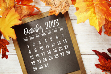 October 2023 monthly calendar with maple leaf on wooden background
