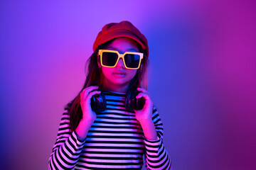 Portrait of a young Asian girl with yellow sunglasses and ear loops around her neck and a red hat with blue and red neon lights.