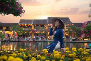 Asian woman is wearing Ao Dai traditional Vietnamese dress and traveling at Hoi An old town in Vietnam.