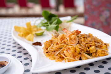 Pad Thai with fresh prawns in a white plate placed on the table in the restaurant.
