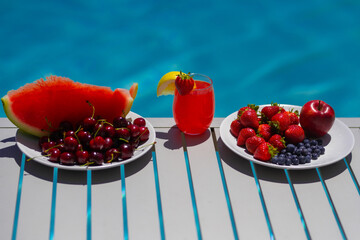 Summer background. Fruit and cocktail on swimming pool background. Healthy food. Outdoor leisure by swimming pool. Summertime. Strawberry, watermelon, cherry and blueberry.