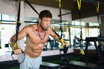 Strong and fit man using trx in gym