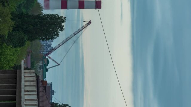 Close-up of the TPP pipe next to the crane. Rain clouds in the background. Trees and unfinished concrete building swaying in the foreground. Movement of the camera from left to right. Vertical video
