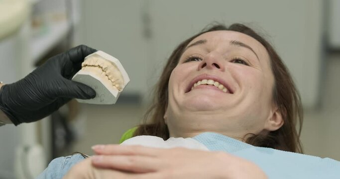 Orthodontist shows cast patient's crooked teeth before braces. Woman laughs at her old crooked teeth. Dental office, successful teeth alignment.