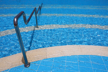Steps for descending into the swimming pool with a metal handrail. Safety for water sports