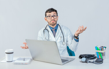 Doctor with laptop with confused expression, clueless raising arms. Young doctor using laptop with confused expression raising arms