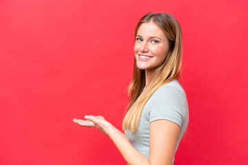 Young beautiful woman isolated on red background extending hands to the side for inviting to come