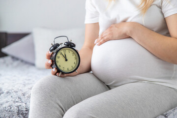 A pregnant woman holds a watch in her hands. Selective focus.