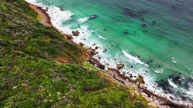 South Africa small beach town Smitswinkel Bay Cape of Good Hope Simon's Town aerial drone cinematic homes surf wave green lush spring summer deep aqua blue ocean cloudy mountain pan down movement