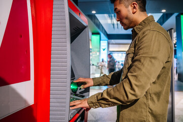Naklejka na ściany i meble Ethnic man using ATM machine in shopping center