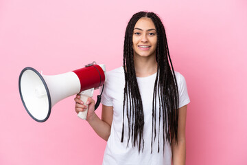 Teenager girl with braids over isolated pink background holding a megaphone and smiling a lot