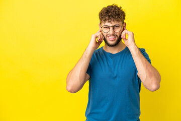 Young handsome caucasian man isolated on yellow background frustrated and covering ears