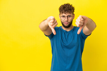Young handsome caucasian man isolated on yellow background showing thumb down with two hands