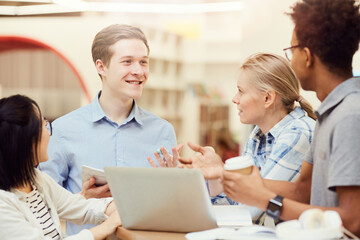 Group of cheerful young multi-ethnic students standing in circle and discussing ideas for project in library