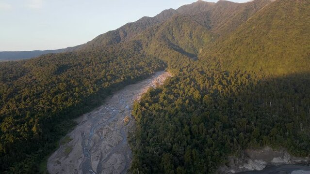 Braided riverbed in lush mountainous landscape at sunset; aerial orbit