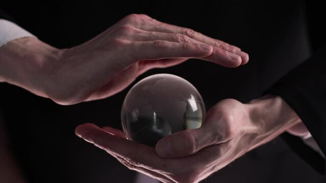 Hands holding a transparent crystal glass ball on a black background