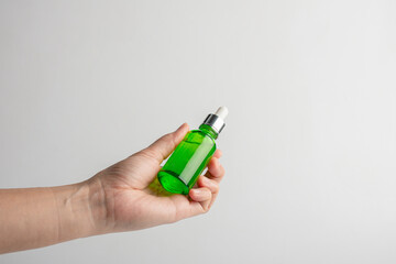 Hand holding up a green glass dropper bottle on white background
