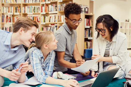 Group of positive young multi-ethnic students studiying in modern library