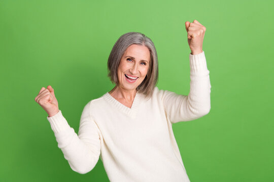 Photo of overjoyed glad pensioner woman react novelty adv raise fists win lottery free tickets trip isolated green background