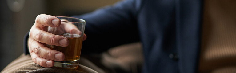 Successful middle aged business man holding glass of alcohol scotch whiskey in his hand while relaxing indoors. Focus on a drink