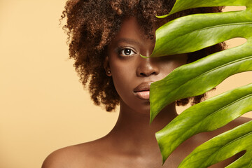Female nude model of african ethnicity with monstera leaf.